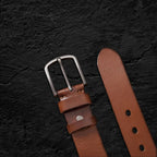 Echtleder-Gürtel aus braunem Rindsleder auf schwarzem Steinfelsen – Detailaufnahme von Schnalle und Gürtelspitze