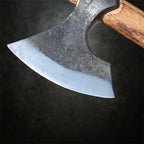 Viking Nord-Axt YXA – detailnaher Blick auf den geschmiedeten Axtkopf mit Holzgriff, rasiermesserscharf geschliffen, präsentiert auf dunklem Schmiedetisch in authentischer Schmiede-Atmosphäre