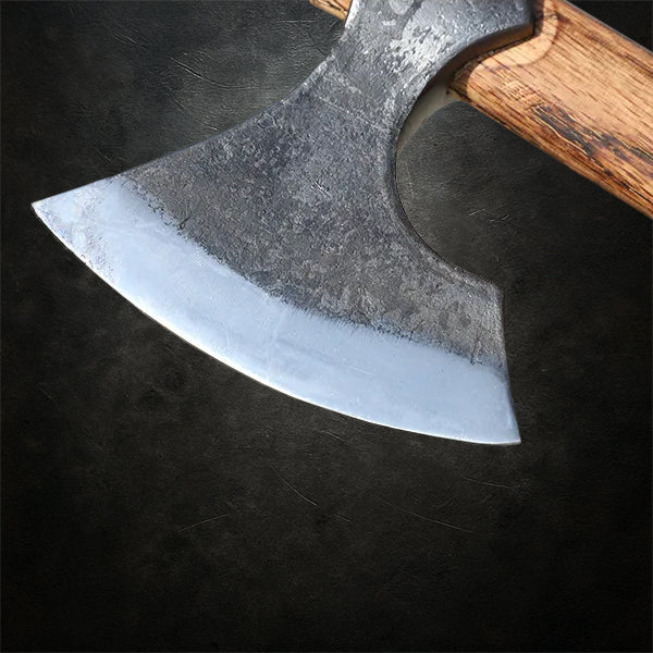 Viking Nord-Axt YXA – detailnaher Blick auf den geschmiedeten Axtkopf mit Holzgriff, rasiermesserscharf geschliffen, präsentiert auf dunklem Schmiedetisch in authentischer Schmiede-Atmosphäre