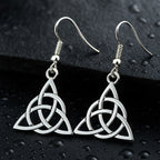 Hochglanzpolierte Triquetra Ohrringe aus Edelstahl auf nassem, dunklem Granit.