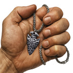 Muskulöse Hand hält eine Wikinger Halskette mit Vegvisir Arrowhead Anhänger aus Metall, detailreich graviert mit nordischem Schutzsymbol.