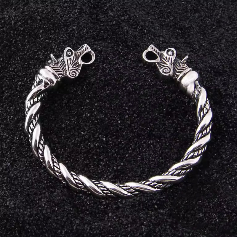 Wikinger Armring aus 925 Sterling Silber mit Drachenkoepfen und gedrehter Flechtung auf schwarzem Sand im nordischen Stil
